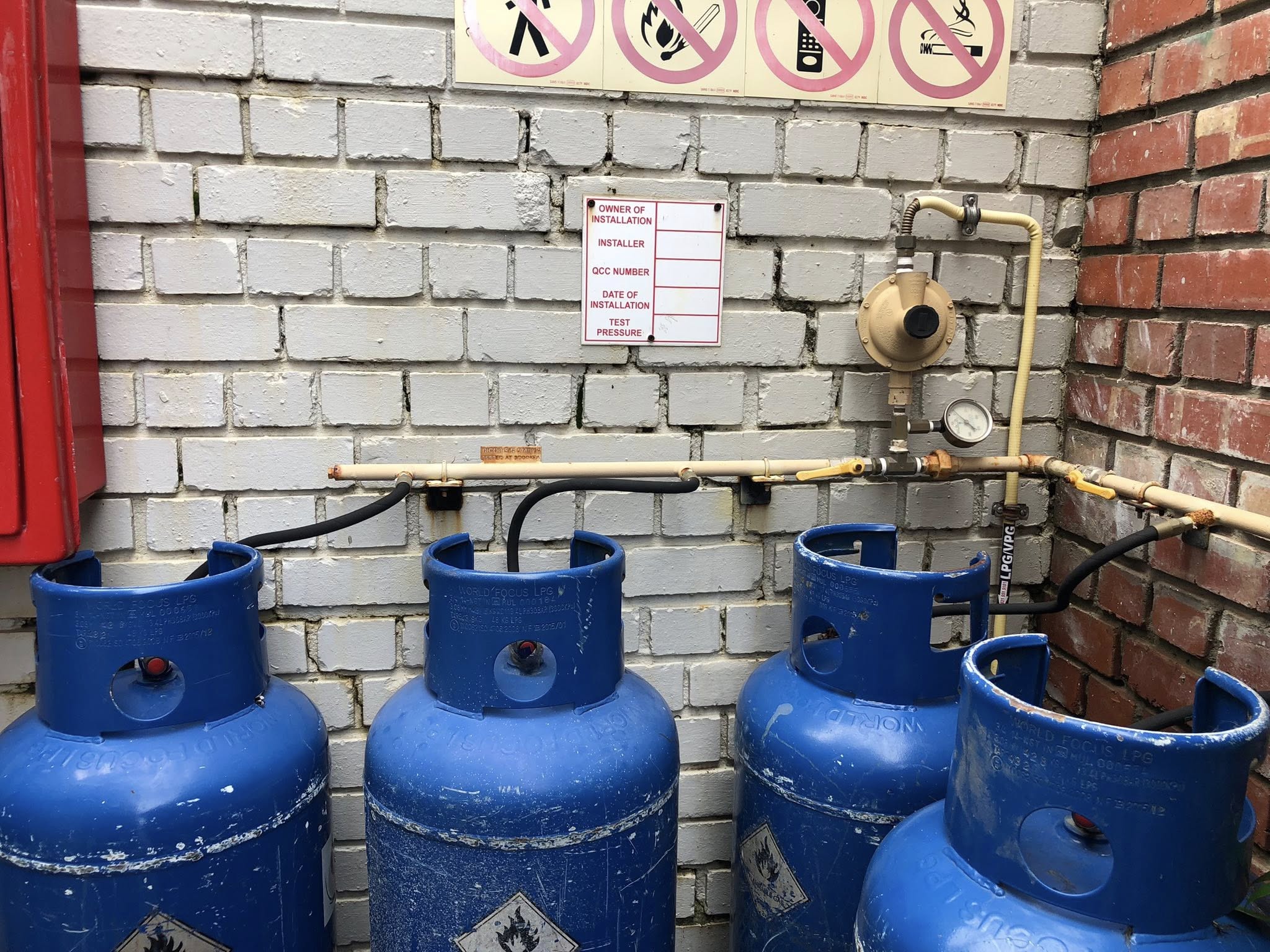 Commercial 4-cylinder LPG bank installed by Red Flame in Cape Town with regulator, piping and compliance plaque.